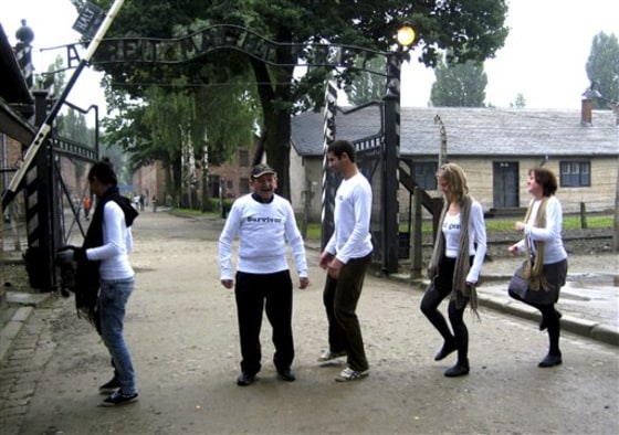 Holocaust survivor Adolek Kohn stands with his grandchildren at the entrance gate to the Auschwitz death camp in Poland in this undated image, taken during the making of a clip in which he is dancing with his family on what easily could have been his own grave.